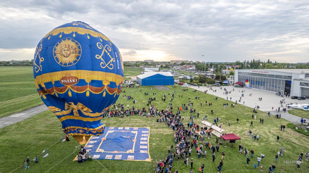 Fotografia przedstawiająca balon lotniczy, który wzbija się do lotu. Wokół niego stoją ludzie.
